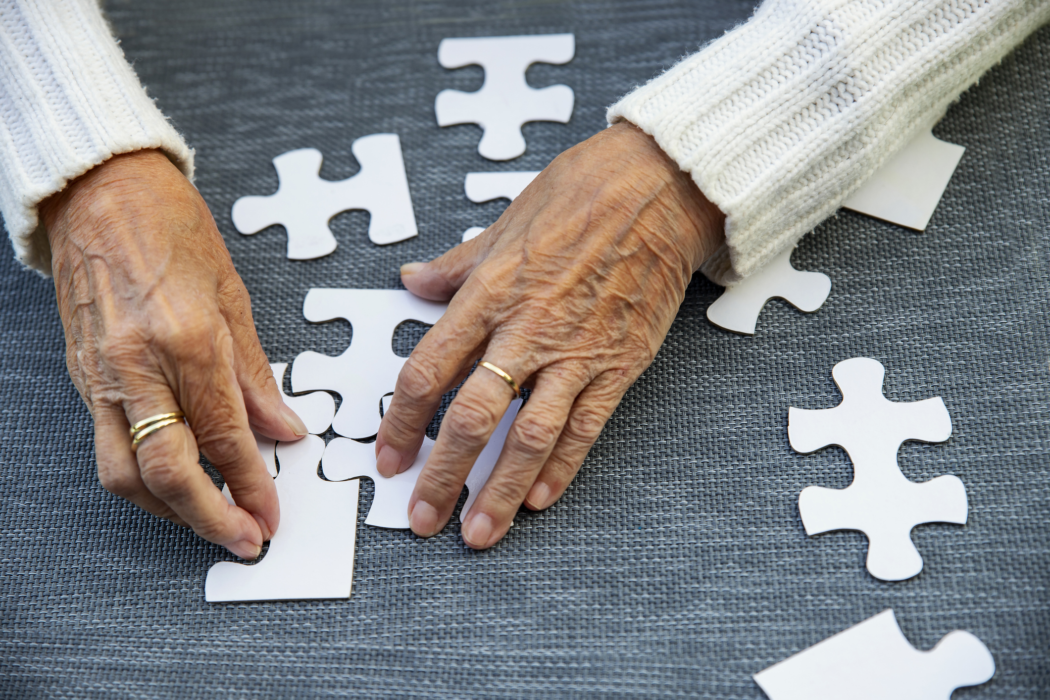 Unknown Old woman playing puzzle game, Matching parts of Jigsaw, white Puzzle pieces on gray table